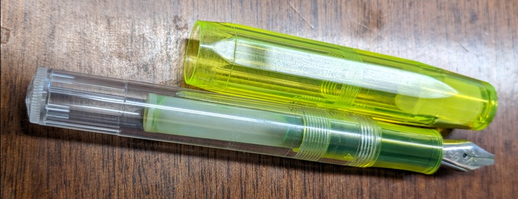 An image of a small fountain pen with a faceted, translucent yellow cap and a transparent body. 